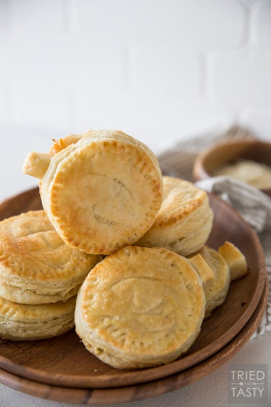 A finished plate of golden brown pumpkin shaped hand pies stacked on top of each other on a wooden brown plate