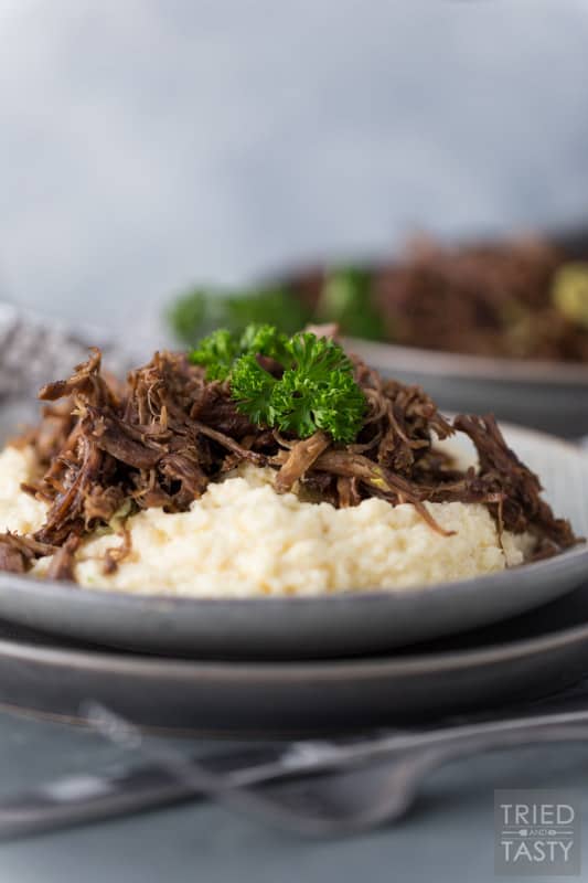 Two plates stacked with mashed cauliflower topped with shredded pot roast garnished with parsley