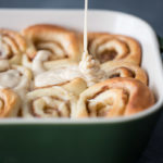 Close up shot of cinnamon rolls being drizzled with maple icing
