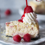 Raspberry sauce drizzled on a slice of Cheesecake Factory White Chocolate Raspberry Truffle Cheesecake on a white plate